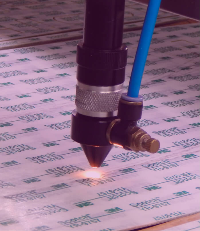 Detalhe de adesivo 3M sendo cortado a laser para aplicações em painéis frontais ou teclados de membrana.